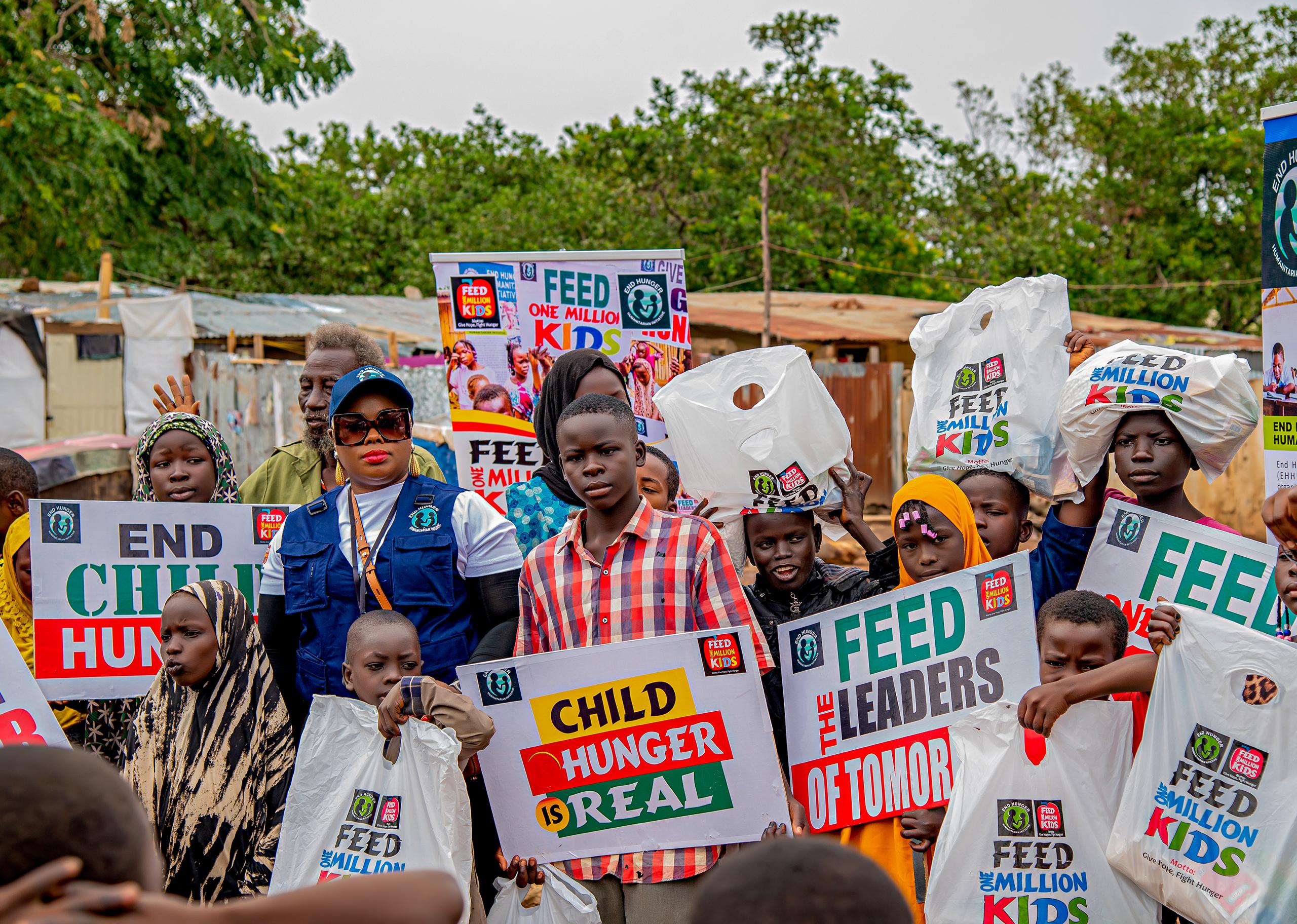 Dr Emem Alban with children and community members at an End Hunger Humanitarian Initiative outreach, holding food packages and anti-hunger campaign signs